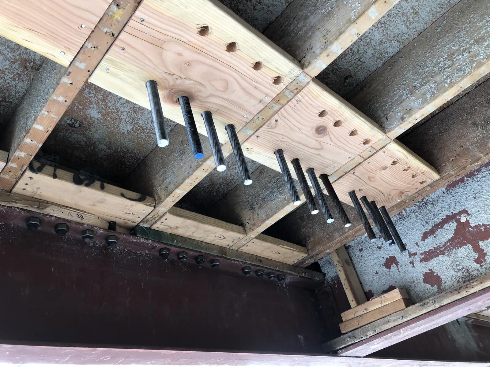 Structural steel-to-wood connection detail: anchor bolts fastening a steel beam to the floor framing of a retrofitted building
