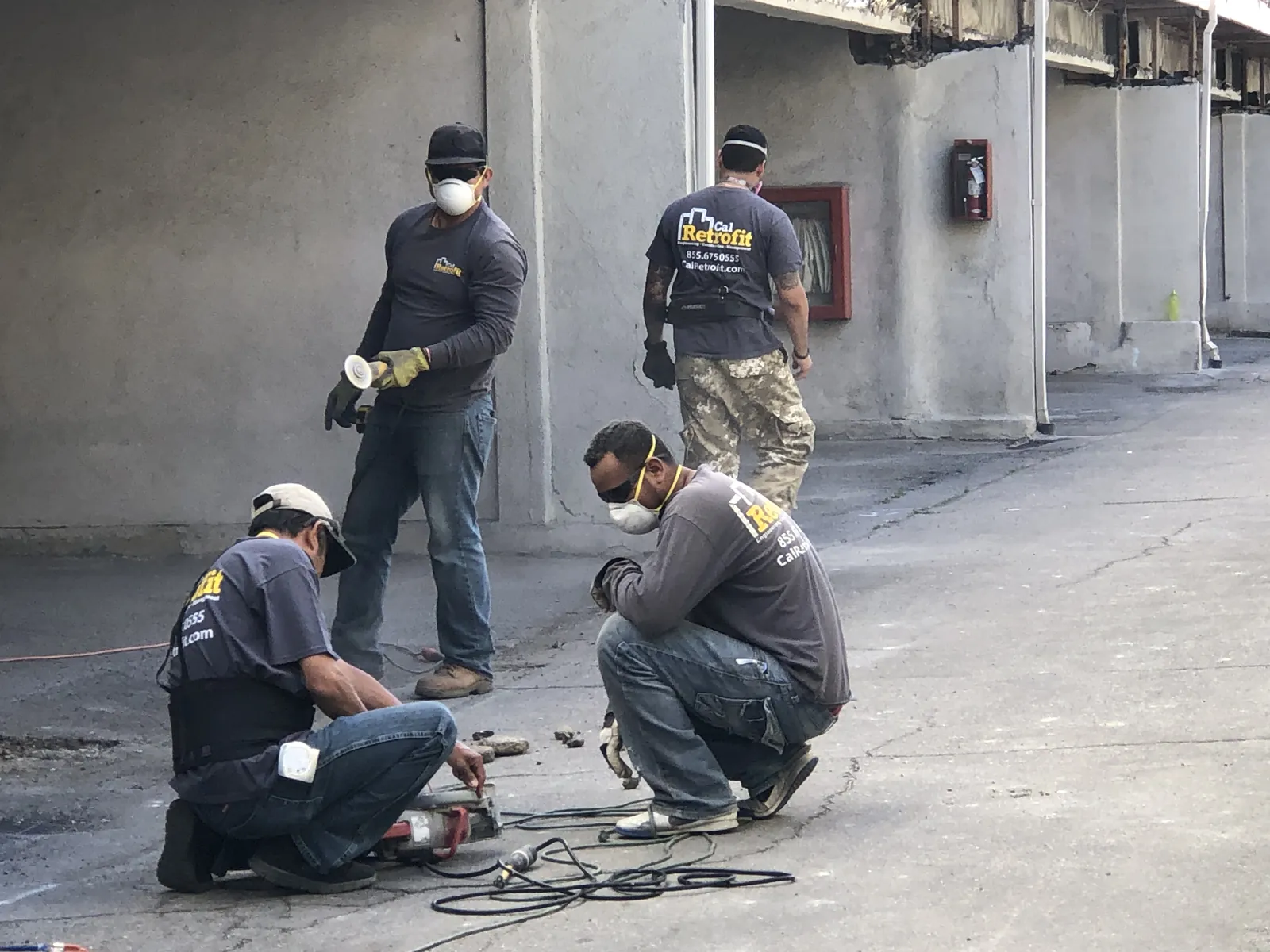 Cal Retrofit field crew in branded shirts coring and anchoring at a soft-story retrofit job site.