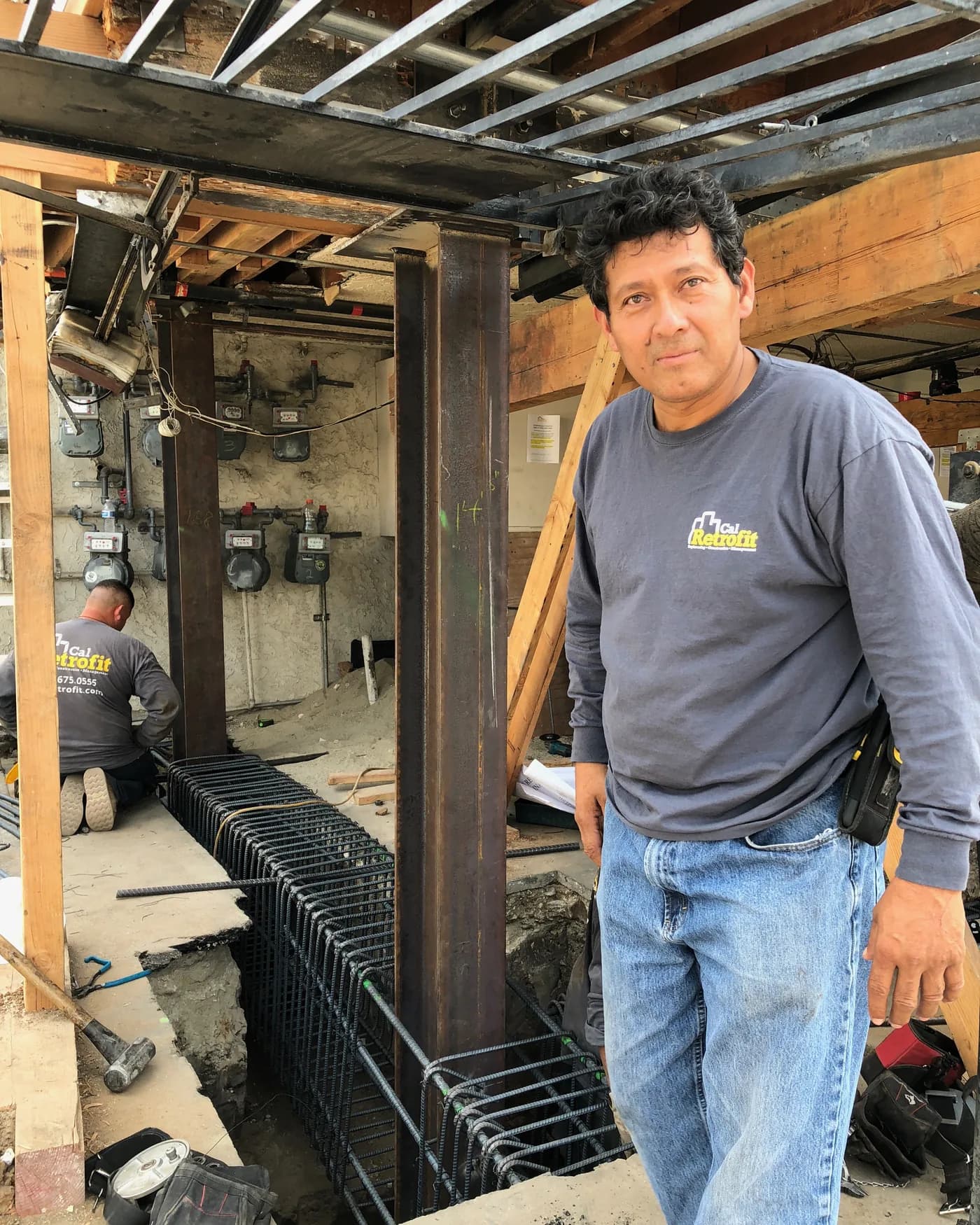 Cal Retrofit foreman on site beside a newly installed steel column and reinforcing-steel footing cage at a soft-story retrofit.