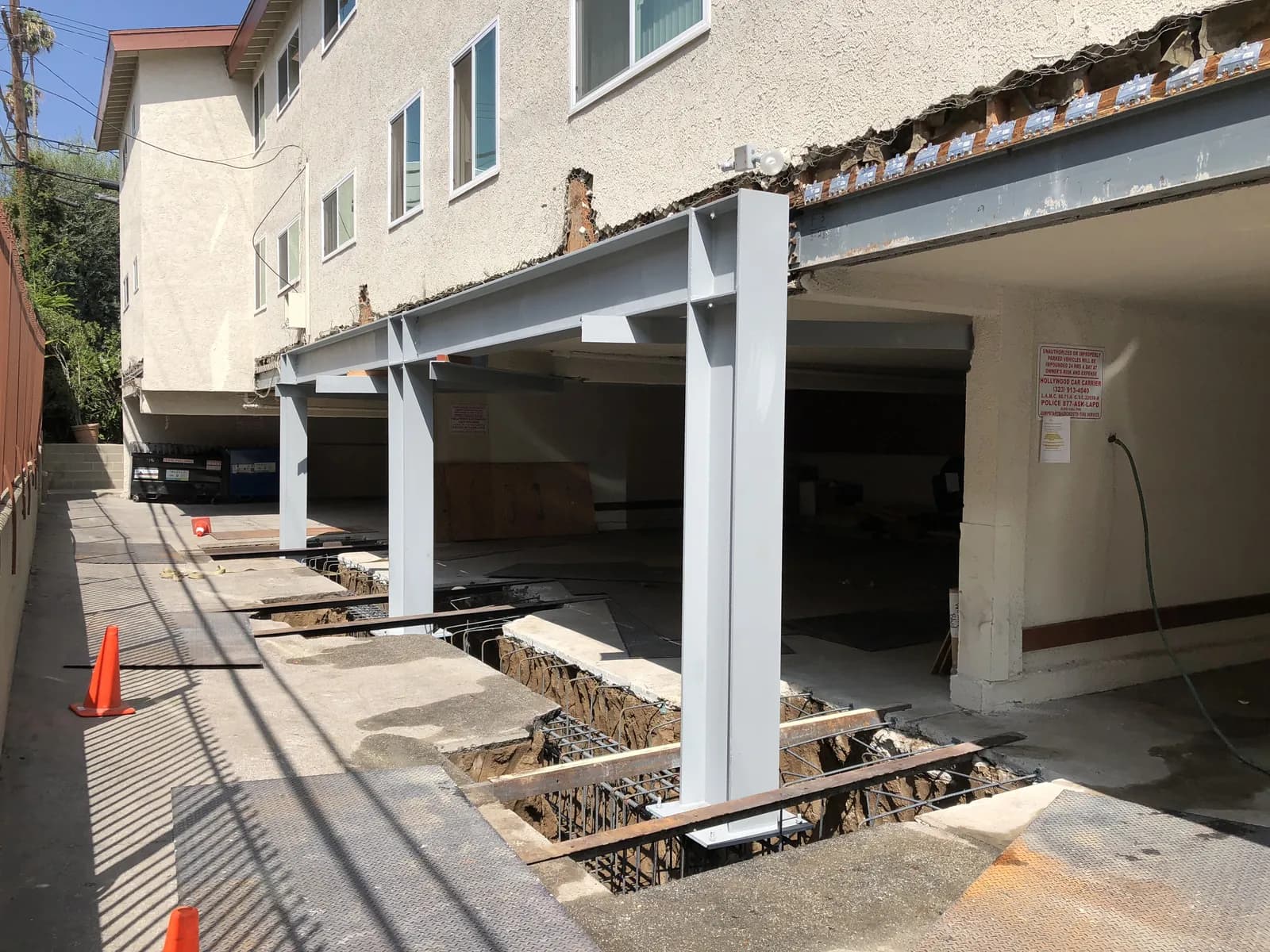 Cal Retrofit soft-story seismic retrofit in progress: new steel moment frames and grade-beam footings replacing the open parking level of a Los Angeles apartment building.